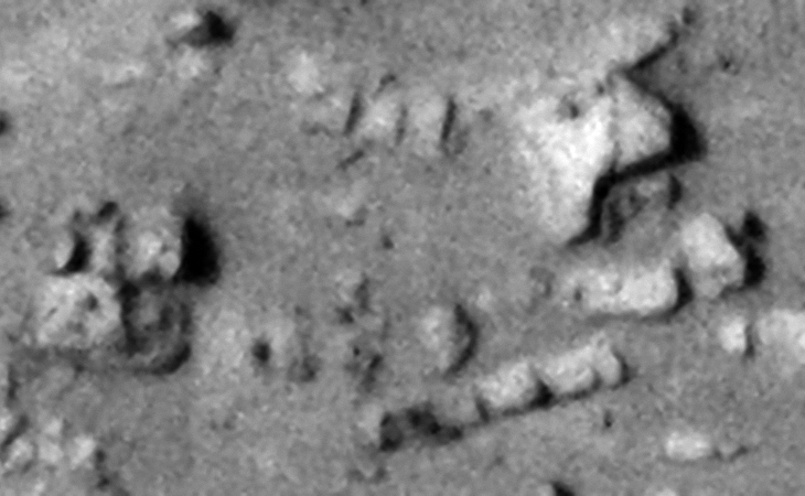Close-up of rows of similar megalithic blocks uniformly spaced, another block with small knob in the center is seen to the left of the image