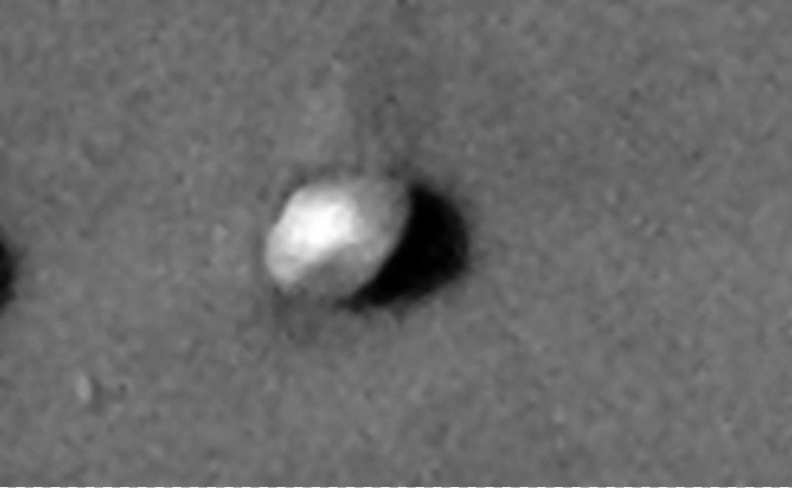 A round, convex shaped object, similar to a classic UFO/saucer dome-shaped craft partially buried in sand