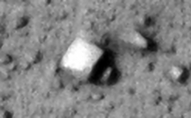 Rectangular megalith or metallic object, note the straight edges and right-angles. One corner seems to be carved out or dented. Note the smaller rectangular part sticking out to the right