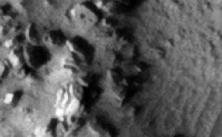 Piece of a sculpture, statue or wreckage? Note the geometric lines and patterns on the surface. A rectangular object with three small features or knobs can be seen to the top