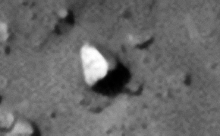 Triangular object with perfectly flat shiny side with perhaps a symbol on the top side