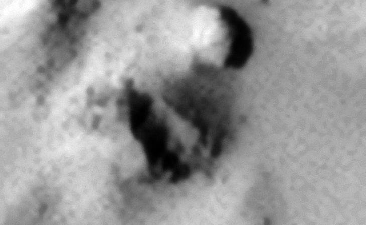 Partially buried parts of a destroyed machine, a bend metallic-plate with what looks like pipes to the left, a rectangular part with pipes in the middle and a disc-like object to the right