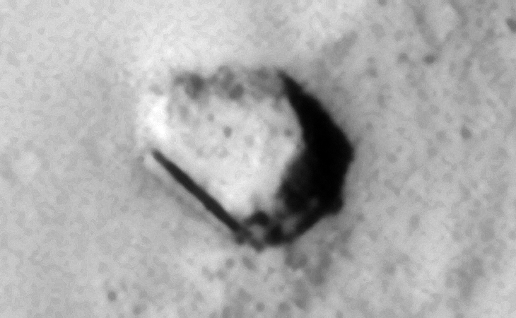 Bent metallic-looking part with a very straight narrow part or pipe to the left, small circular object to the middle bottom